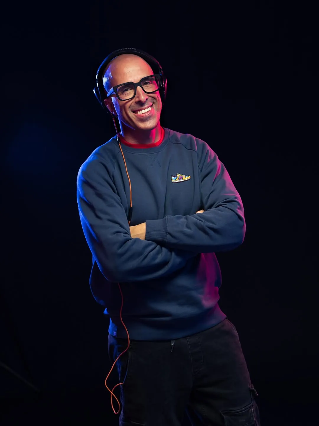 Retrat fosc amb els braços creuats i llum magenta sobre una jaqueta esportiva.