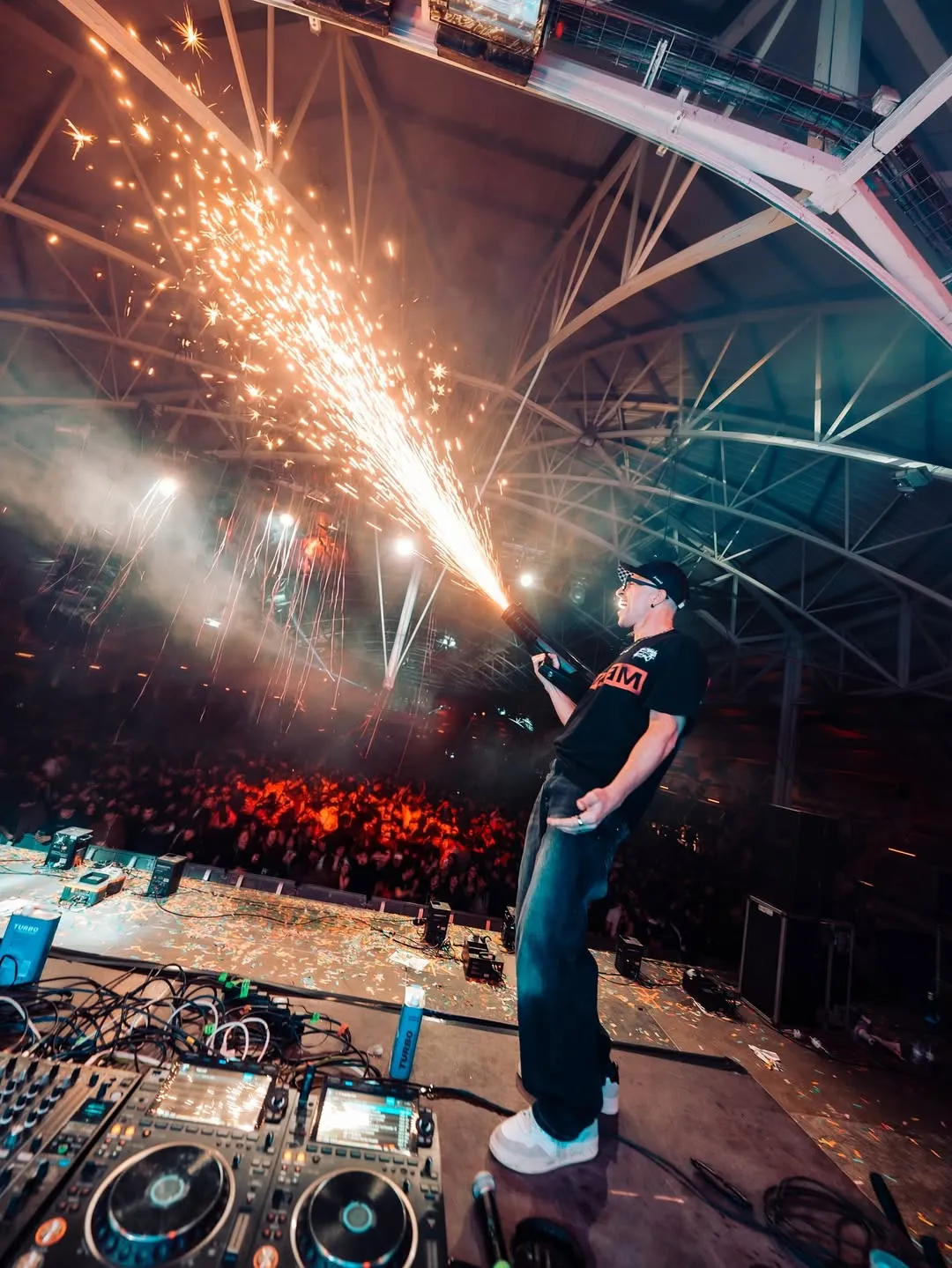 Escena oberta de sala amb foc vertical i públic sota una estructura industrial.