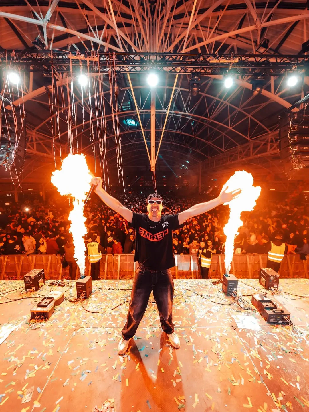 MON DJ centrada entre dues columnes de foc en un pla frontal de tancament.